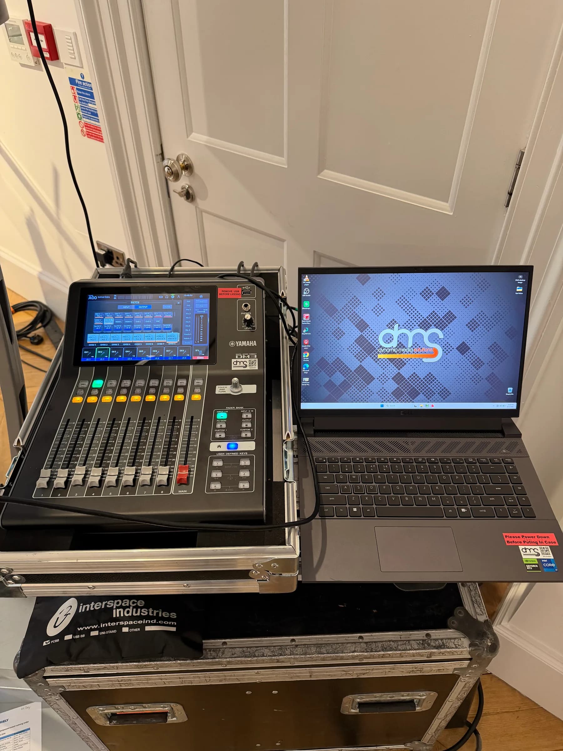 Audio mixing console beside a laptop displaying the DMS logo on stacked flight cases