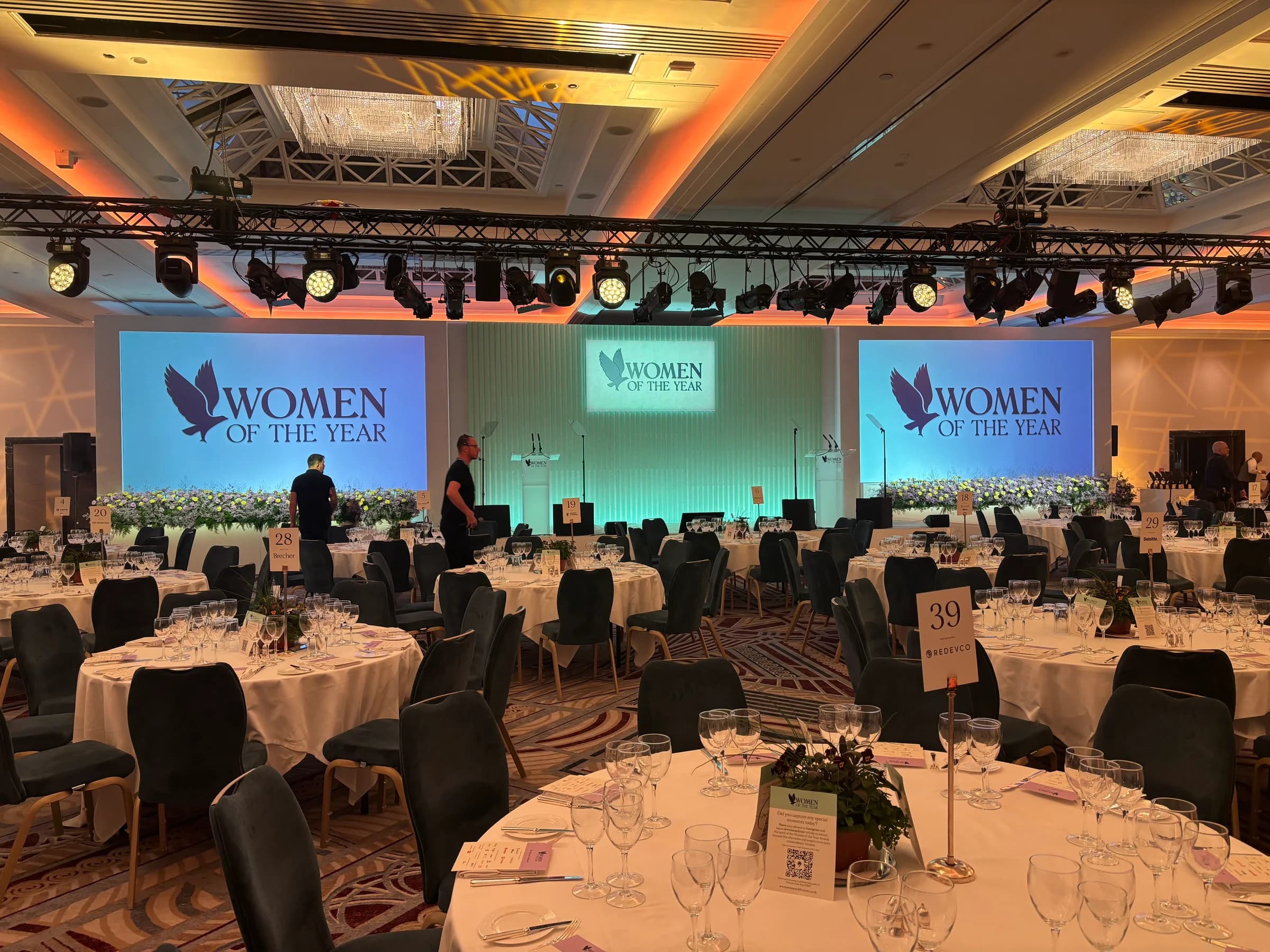 Prepared dining tables facing the Women of the Year stage and screens under green and amber lighting