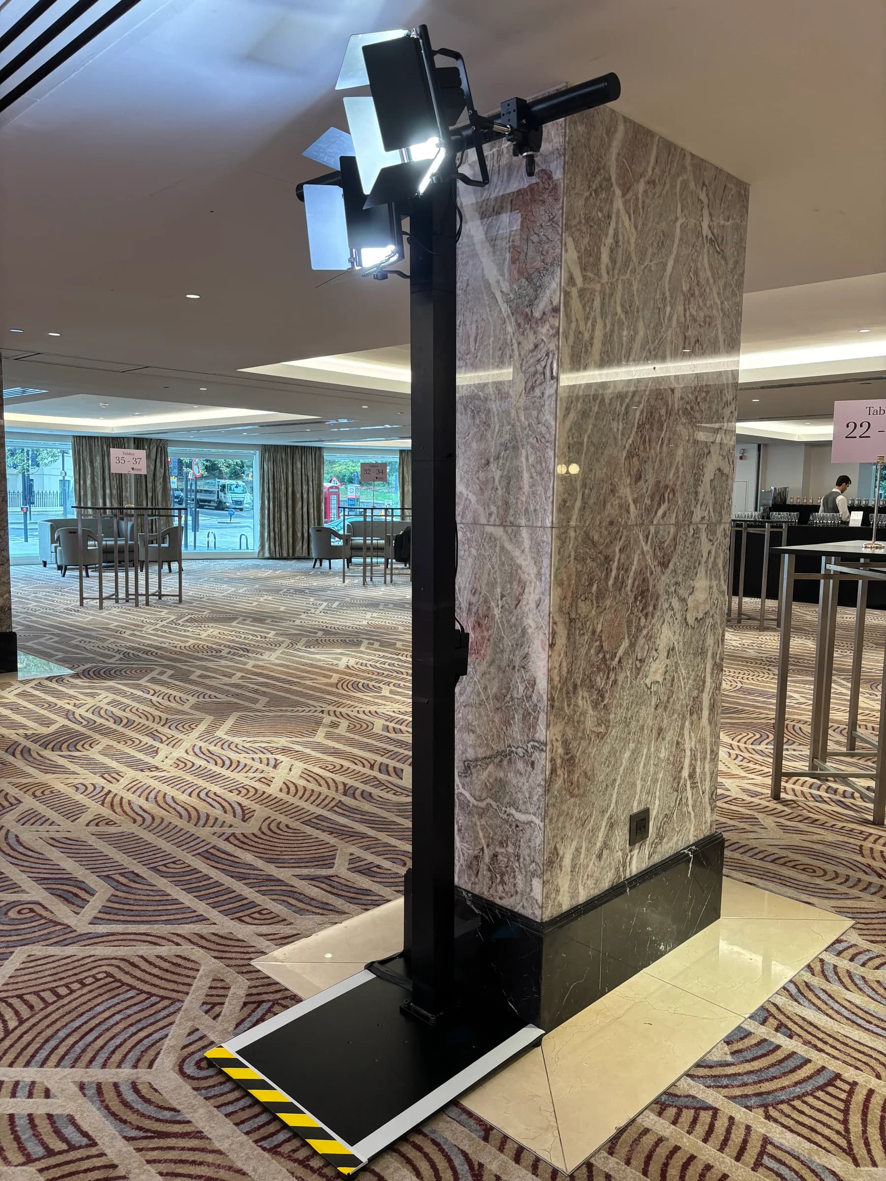 Two illuminated lighting fixtures on a black stand beside a marble pillar
