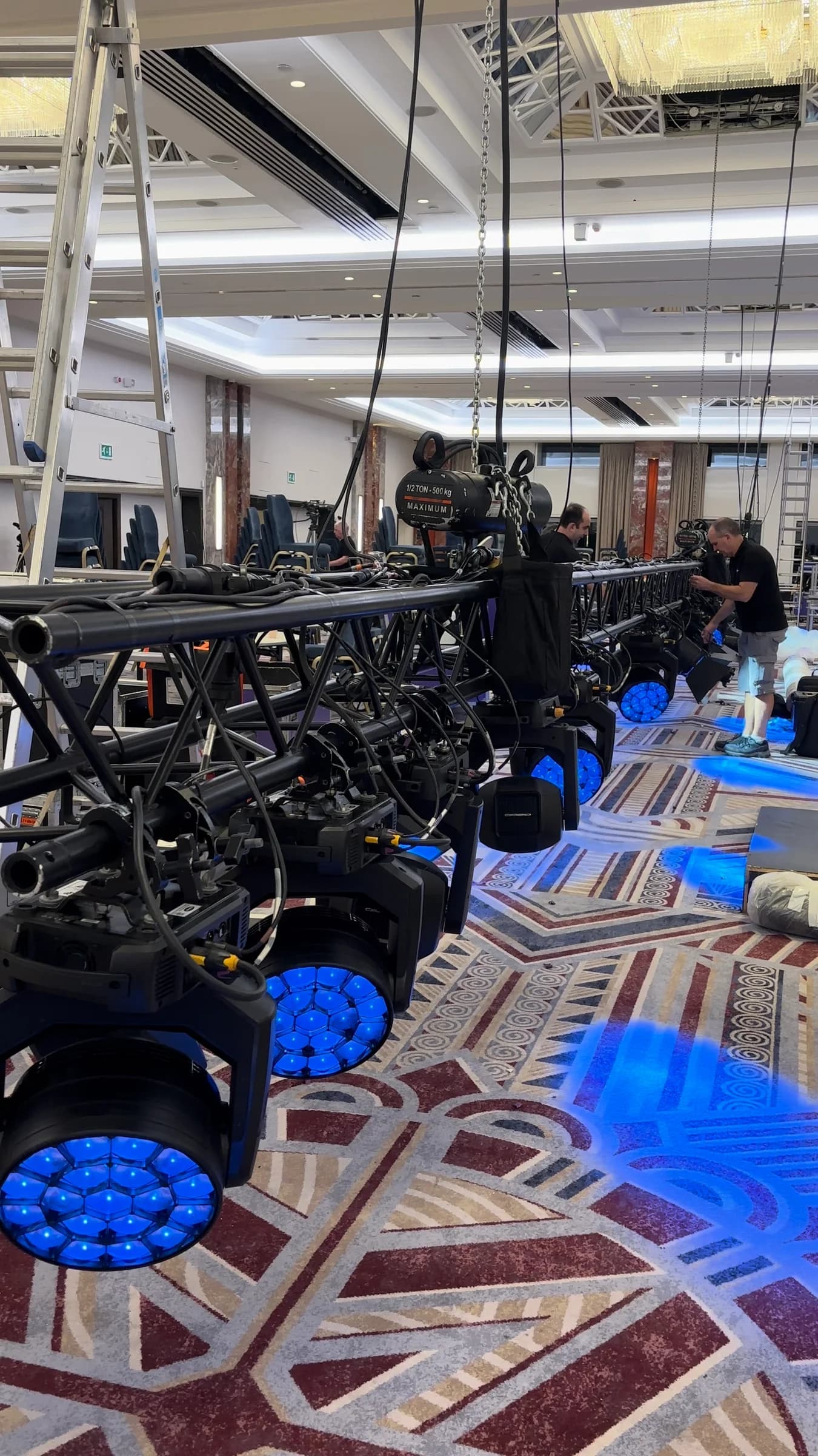 Crew checking blue-lit fixtures and cabling on a lowered lighting truss