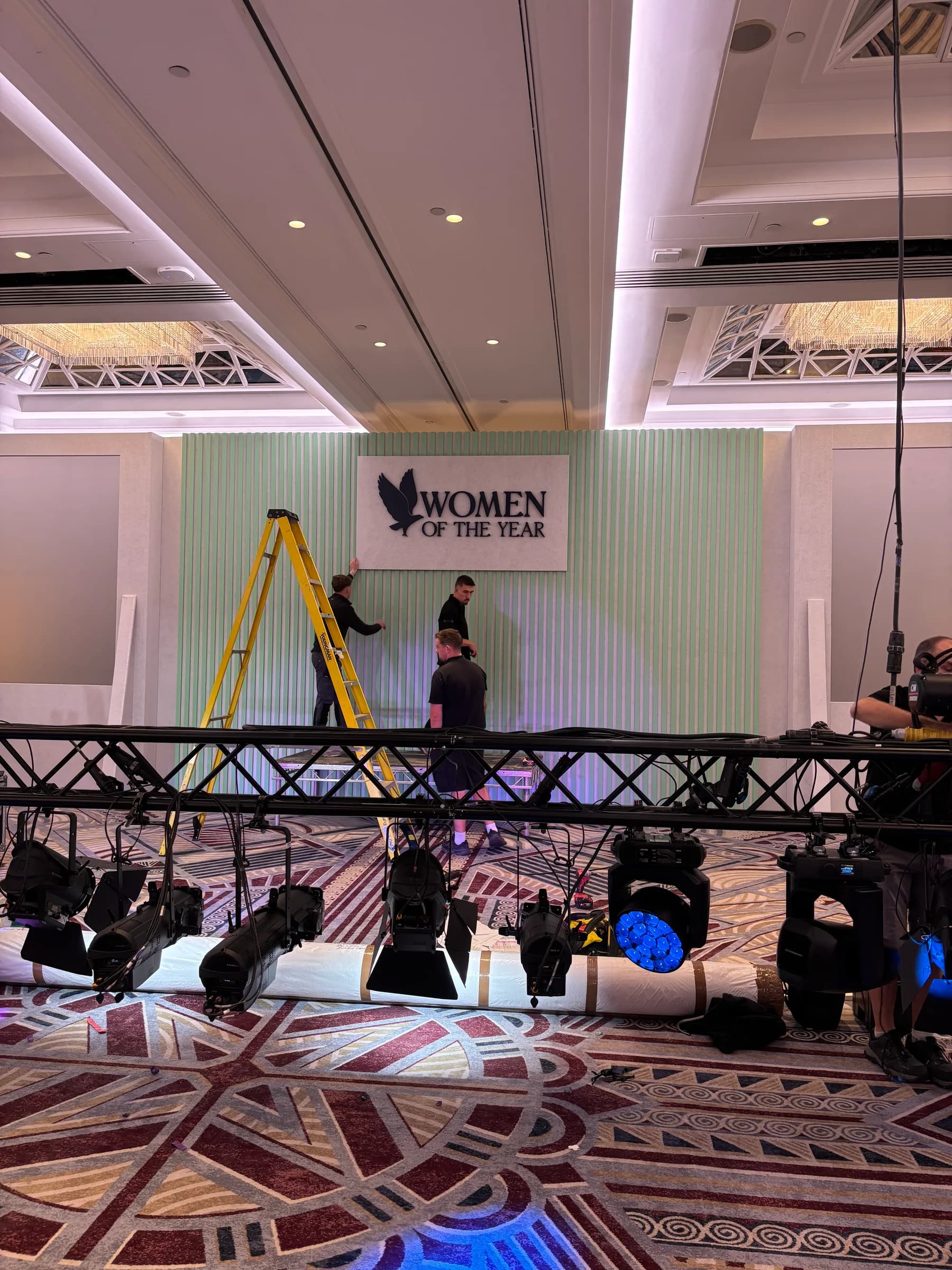 Lighting fixtures on a lowered truss in front of the Women of the Year stage backdrop