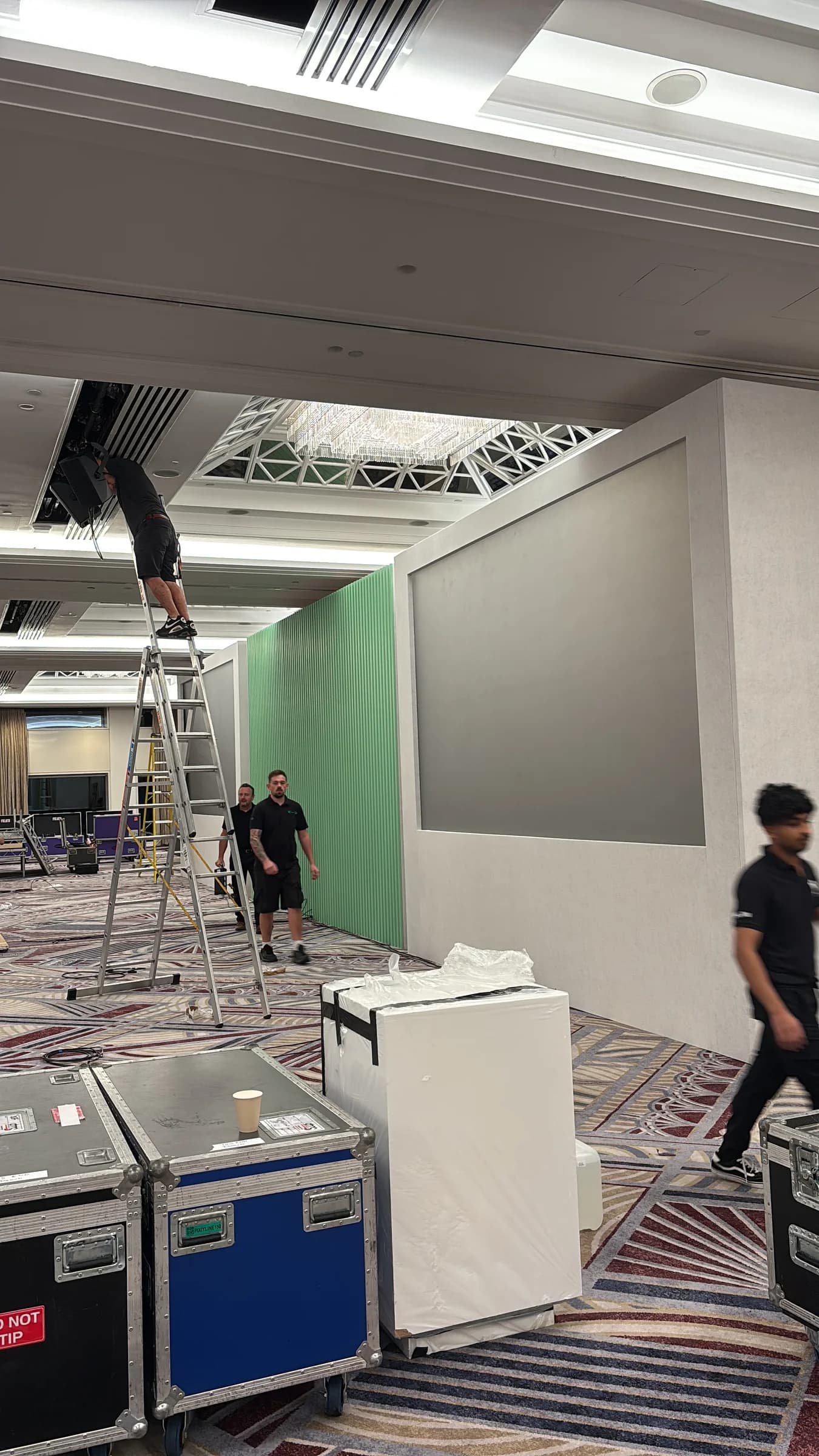 Crew and ladders beside the green and white stage backdrop during installation